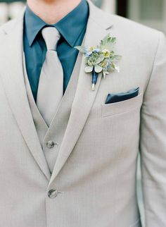 a man in a gray suit with a blue tie and flower boutonniere