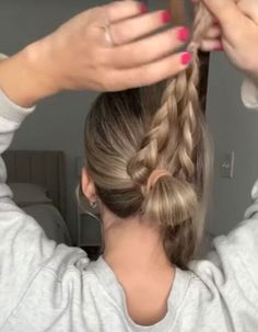 a woman is braiding her hair in a ponytail