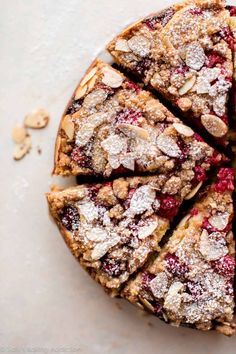 a cake with powdered sugar and berries on top is cut into slices to show the filling