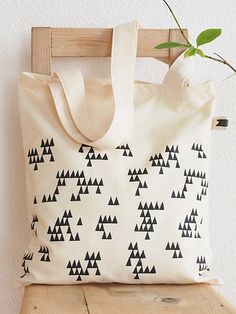 a white tote bag sitting on top of a wooden chair next to a plant