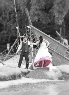 a man and woman dressed in wedding attire standing on a bridge with their arms around each other