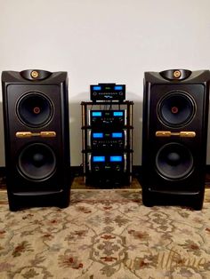 two large speakers sitting next to each other on top of a carpeted floor in front of a wall