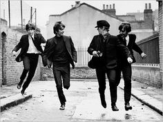 the beatles running down an alley way in black and white, with brick buildings behind them