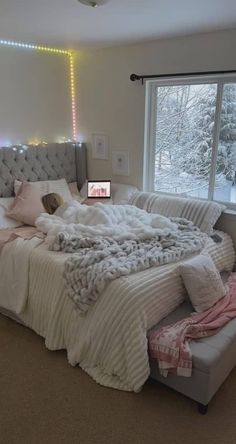 a bedroom with a large bed and lots of blankets on the top of it, in front of a window