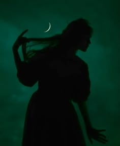 a woman with long hair standing in front of a dark green background and the moon behind her