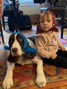 two small children sitting on the floor with a dog wearing a bandanna around their head