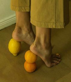 a person standing next to two oranges on the floor with their feet propped up