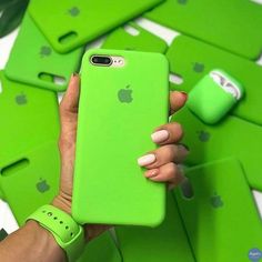 a woman holding an apple phone in her hand with green cases on the ground behind her