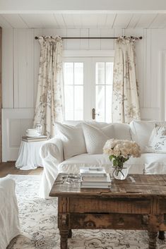 a living room filled with white furniture and flowers on top of a wooden coffee table