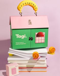 a green and pink toy house sitting on top of stacks of books with a banana hanging from the roof