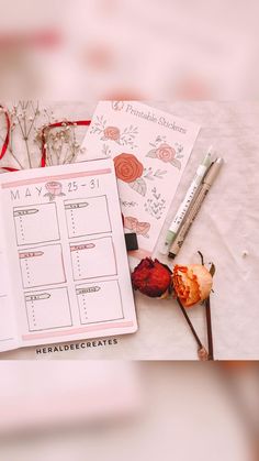 an open planner sitting on top of a table next to some flowers and pencils