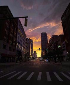 the sun is setting over a city street with tall buildings and traffic lights on both sides