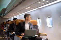 a man sitting on an airplane with his laptop in front of him and other people behind him