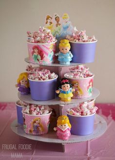 there is a tiered cake with cupcakes and princesses on the top