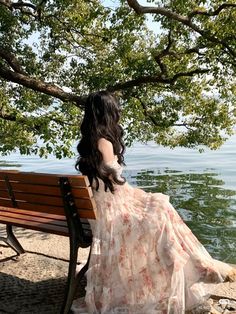 a woman is sitting on a bench by the water