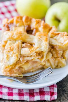 a white plate topped with apple pie next to an apple on a red and white checkered table cloth