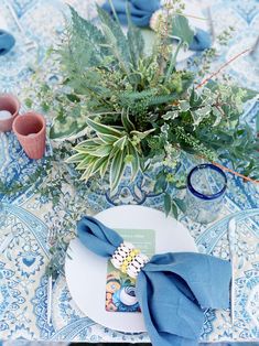 a blue and white place setting with succulents, greenery and napkins