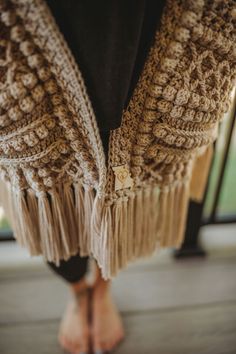 the legs of a woman wearing sandals and a crocheted shawl with fringes