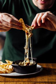 a man is eating some food from a bowl on a table with chips and sauce