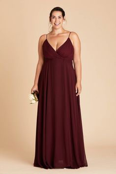 a woman in a long dress smiling and holding a bouquet on her hand, wearing a dark red bridesmaid gown