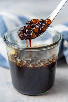 a spoon with some food in it on top of a glass jar filled with liquid