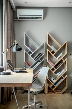 a desk with a laptop and bookshelf in the corner next to a window