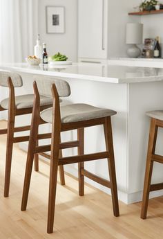 three wooden stools sitting in front of a kitchen island with marble counter tops and white walls