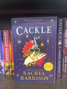 three books on a shelf in a library, one is called cackle by author rachel harrison