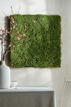 a table with a vase and some flowers on it next to a moss covered wall