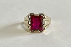 Handsome vintage 10k yellow gold 1940s era ring featuring a vibrant created ruby! The deep red gem weighs an estimated 6 carats, is emerald cut, and securely bezel set. The substantial setting is detailed with a decorative design on the shoulders. Charming vintage piece of fine jewelry for him or her, featuring July's birthstone! ERA - Circa 1950 METAL / MATERIAL - 10k yellow gold, 1 created ruby (estimated 6 carats) [Synthetic ruby contains essentially the same chemical composition & properties Antique Red 14k Gold Signet Ring, Antique Red Signet Ring In 14k Gold, Red Rectangular 14k Gold Ring, Vintage Ruby Rings With Polished Finish, Vintage 14k Gold Ruby Ring With Polished Finish, Classic 14k Gold Red Signet Ring, Classic Red 14k Gold Signet Ring, Antique Red Ruby Ring In 14k Gold, Classic Red Signet Ring Stamped 14k