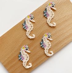 four little seahorses made out of beads on a piece of wood with white background