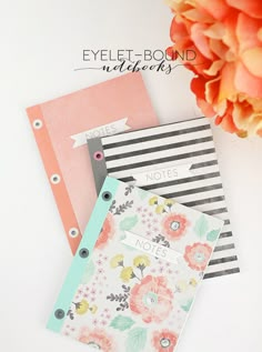 three notebooks sitting next to each other on top of a white table with flowers