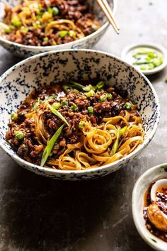 two bowls filled with noodles and vegetables on top of a gray table next to sauces