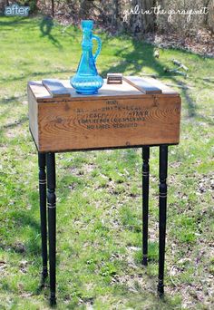 an old wooden box with writing on it is sitting in the grass near a blue vase