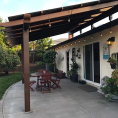 an outside patio with table, chairs and lights on the side of the house that is covered by a pergolated roof