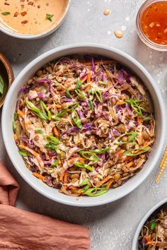 a white bowl filled with coleslaw slaw next to bowls of dipping sauces