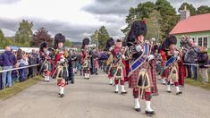 some men in kilts are marching down the street with people standing around watching them