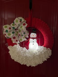 a wreath with a snowman on it hanging from the front door, next to a red door