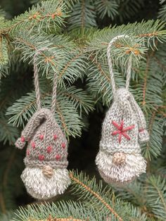 two knitted christmas ornaments hanging from a pine tree's needles with red and white stars on them