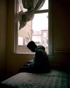 a man sitting on top of a bed next to a window