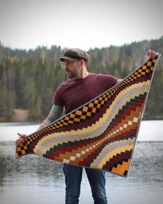 a man is holding a quilt over his shoulder by the water with trees in the background