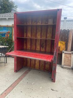 a red bench sitting in front of a wooden book case on top of a sidewalk