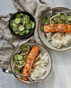 two plates with salmon, rice and cucumbers on them next to a fork