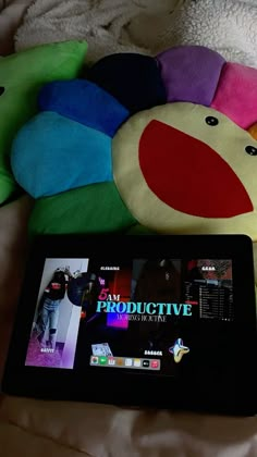 a tablet sitting on top of a bed next to a colorful stuffed animal and toy