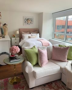 a bedroom with a white couch, pink and green pillows, and a large window