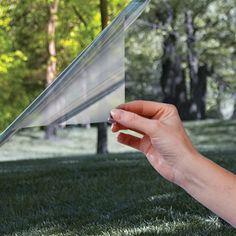 a person holding up a piece of paper in front of a window with trees outside