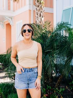 a woman standing in front of a palm tree wearing shorts and a tank top with her hands on her hips