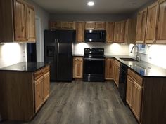 an empty kitchen with black appliances and wood cabinets in the middle, light from recessed lighting is on