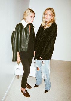 two women standing next to each other in front of a white wall wearing black leather jackets