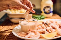 someone dipping shrimp into a small bowl of sauce on a plate with other food items